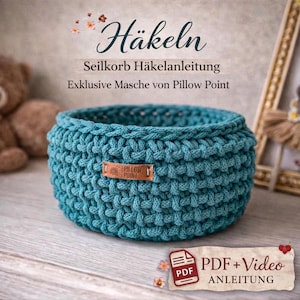 May include: A teal crocheted basket with a textured stitch. The basket features a small, rectangular leather tag with the text "Pillow Point". The image also includes text that says "Häkeln", "Seilkorb Häkelanleitung", and "PDF + Video Anleitung".