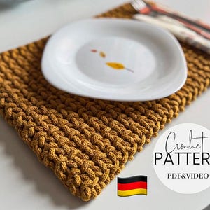 May include: A mustard-coloured, square crochet placemat with a white plate on top. The plate has a simple leaf design. The image also includes a fork and knife, and a round sticker with the words "Crochet Pattern" and "PDF & VIDEO".