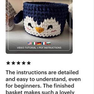 May include: A handmade crochet penguin basket in navy blue and white. The basket has a penguin face design with black eyes, a yellow beak, and pink cheeks. The text "CROCHET PENGUIN BASKET PATTERN" is at the top.