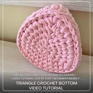 May include: A light pink, triangular crochet bottom, tightly woven to create a textured surface. The image features the text "TRIANGLE CROCHET BOTTOM VIDEO TUTORIAL". The item is likely handmade.
