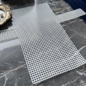 Peut inclure: Feuilles de canevas en plastique blanc avec un motif quadrillé. L'une est rectangulaire, l'autre a une forme de croix avec une poignée. Les feuilles sont sur une surface en marbre.