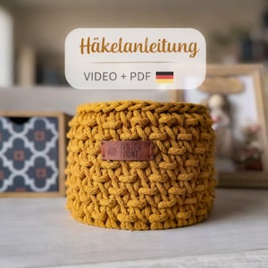 Peut inclure: Panier crocheté jaune moutarde avec une texture tissée. Une étiquette en cuir marron avec le texte "PILLOW POINT" est attachée à l'avant. L'image comprend également le texte "Häkelanleitung VIDEO + PDF".