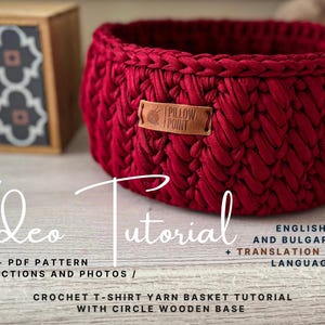 Puede incluir: Una cesta roja de ganchillo hecha a mano con una etiqueta de cuero que dice "PILLOW POINT". La cesta está hecha de hilo grueso y tiene forma circular. La imagen también incluye el texto "Video Tutorial" y "Crochet T-shirt Yarn Basket Tutorial".