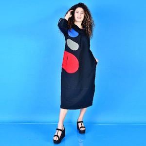 May include: A black long-sleeved dress with a cowl neck and colorful abstract design. The dress has a loose fit and falls to the knees.