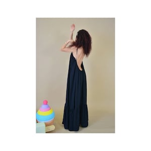 May include: A long, navy blue maxi dress with spaghetti straps and a low back. The dress has a tiered, ruffled hemline. A colorful, toy-like object is in the foreground.