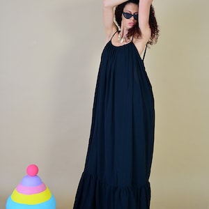 May include: A long, flowing navy blue maxi dress with spaghetti straps and a ruffled hem. The dress is worn with sunglasses and a necklace. A colorful toy is in the background.