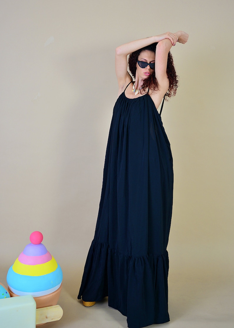 May include: A long, flowing navy blue maxi dress with spaghetti straps and a ruffled hem. The dress is worn with sunglasses and a necklace. A colorful toy is in the background.