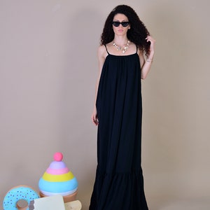 May include: A black maxi dress with spaghetti straps and a ruffled hem. The dress is worn by a person wearing sunglasses and a necklace. Decorative ice cream and donut props are in the foreground.