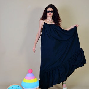 May include: A long, flowing black dress with thin straps and a ruffled hem. The dress is worn with sunglasses and a necklace. Decorative ice cream and donut props are in the foreground.