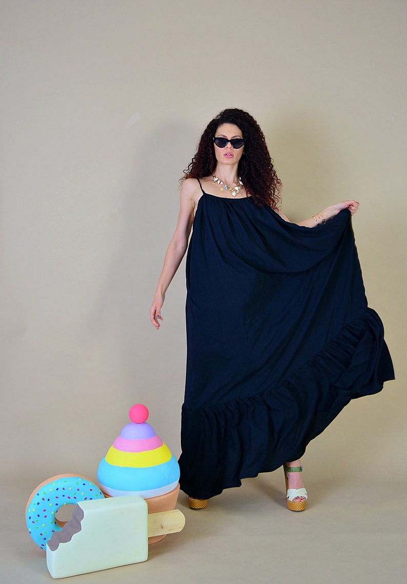 May include: A long, flowing black dress with thin straps and a ruffled hem. The dress is worn with sunglasses and a necklace. Decorative ice cream and donut props are in the foreground.