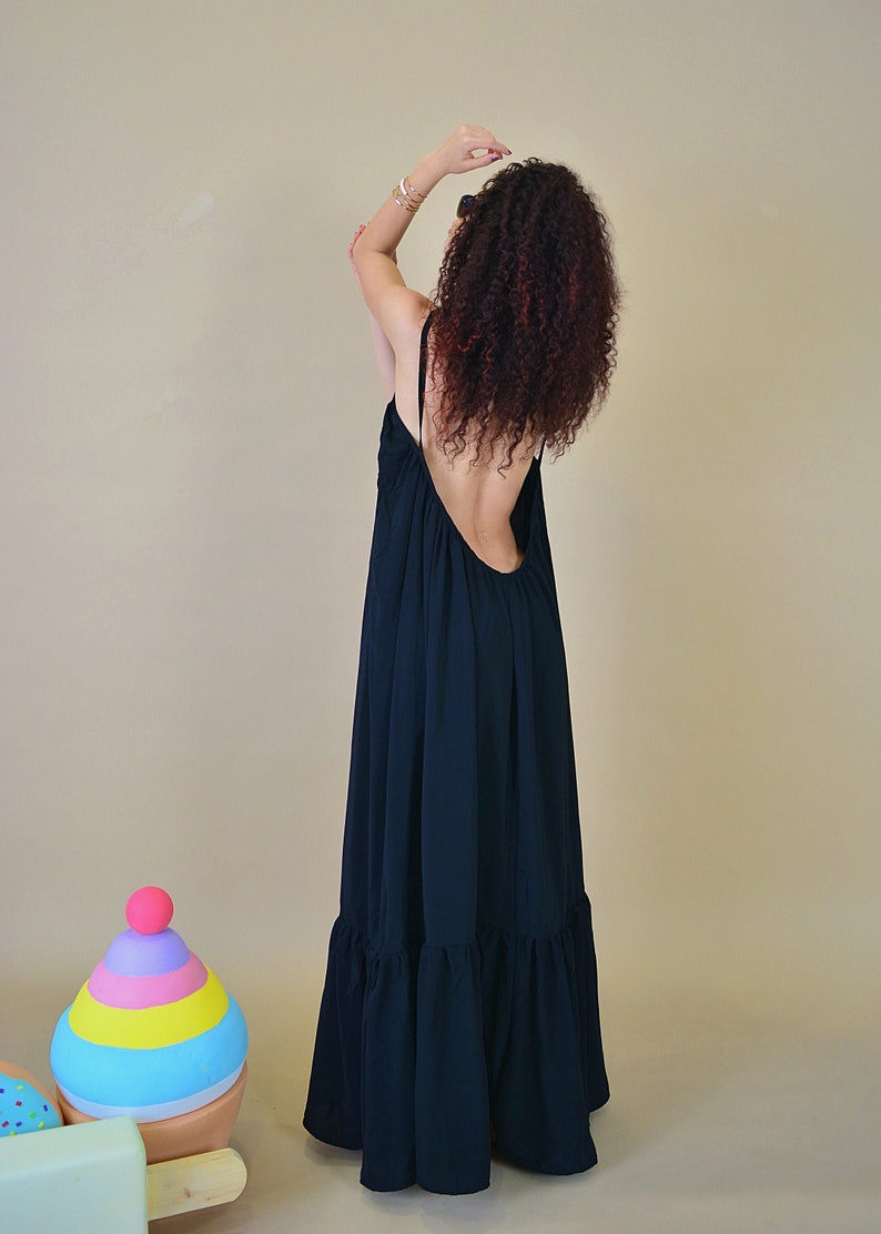 May include: A long, flowing black dress with a low back and spaghetti straps. The dress has a ruffled hemline and is worn by a person with curly red hair. A colorful ice cream cone prop is in the foreground.