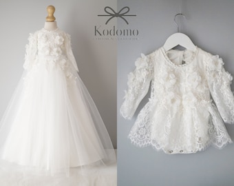 May include: White lace baby dress with long sleeves and a floral design. The dress has a tulle skirt and is perfect for a special occasion.