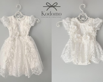 May include: Two white lace dresses for baby girls, one long and one short, hanging on white hangers. The dresses have delicate lace detailing and ruffles.