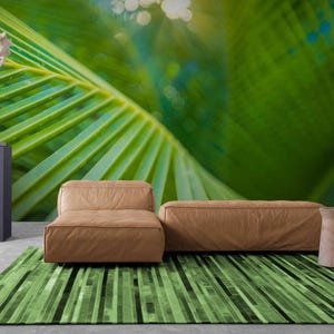 May include: Two brown leather couches with a green striped rug in front of them. The background is a blurry image of green palm leaves.