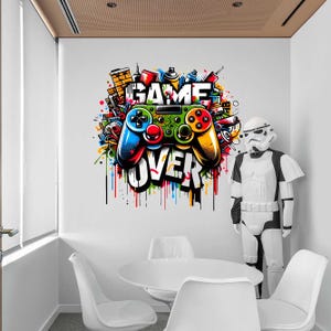 Puede incluir: Un colorido mural que muestra un mando de videojuegos con las palabras "GAME OVER". El mando es azul, verde y amarillo, con un fondo de estilo grafiti. También hay una figura de Stormtrooper.
