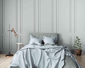May include: A bedroom scene featuring a bed with light blue bedding, including a duvet and pillows. The room has light gray walls with paneling, a wooden floor, and a floor lamp with a copper finish. A small potted plant sits on the floor.