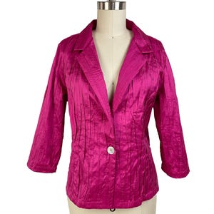 May include: A bright fuchsia blazer with a single white button. The jacket has a notched collar, three-quarter sleeves, and vertical pleating. The garment is displayed on a mannequin against a white background.