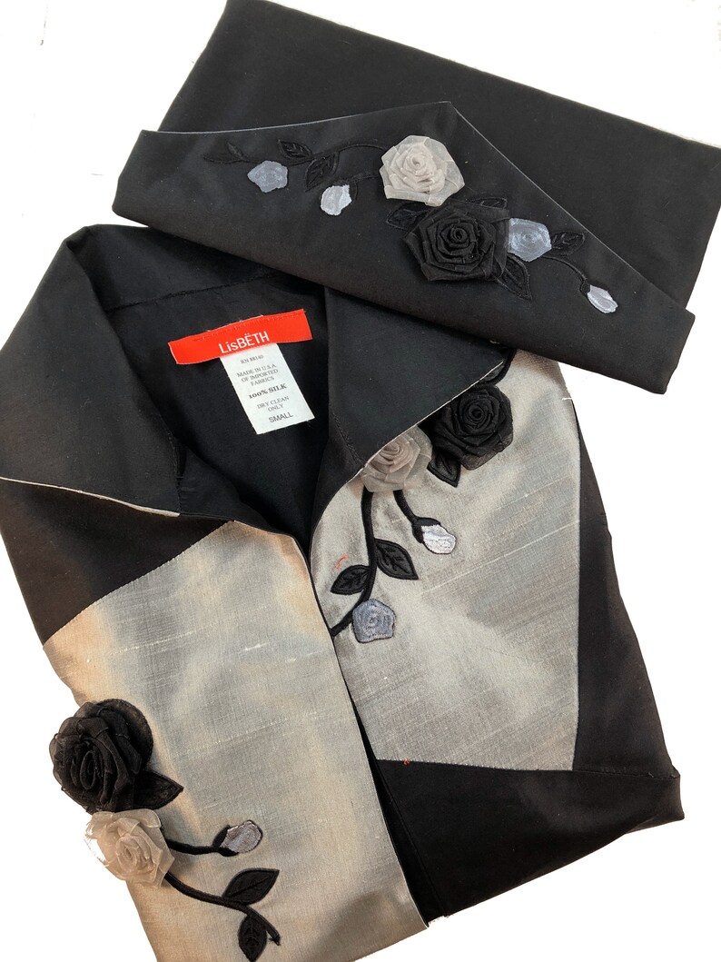 May include: A black and silver silk blouse with a black collar and a decorative rose design. The blouse has a label that reads "Lisbeth" and "100% Silk".