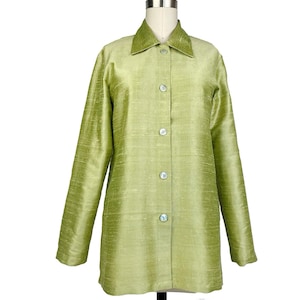 May include: A light green long-sleeve button-down shirt with a pointed collar and a textured, slubbed fabric finish. The garment features five round, iridescent buttons down the center front placket and long sleeves with straight cuffs.
