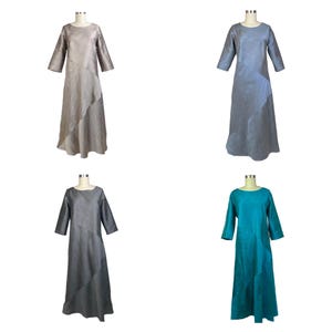 May include: Four long-sleeved dresses displayed on mannequins, each featuring a round neckline and a diagonal seam across the front. The dresses are available in four distinct solid colors: beige, light blue, dark gray, and teal green.