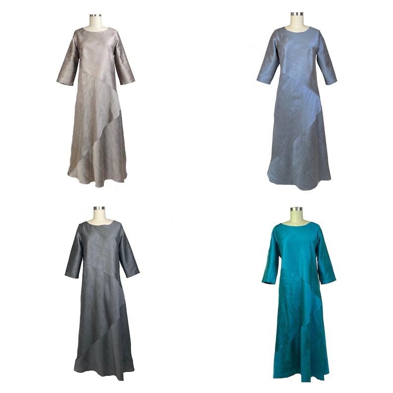 May include: Four long-sleeved dresses displayed on mannequins, each featuring a round neckline and a diagonal seam across the front. The dresses are available in four distinct solid colors: beige, light blue, dark gray, and teal green.