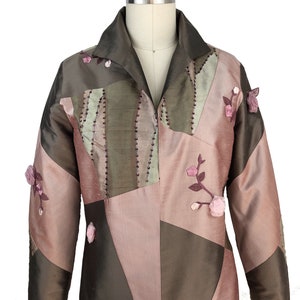 K&ouml;nnte beinhalten: Eine braune und rosafarbene Patchworkjacke mit Blumenstickerei. Die Jacke hat einen Kragen und lange &Auml;rmel.