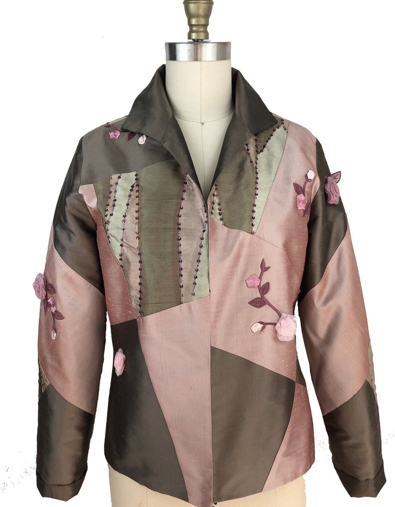 K&ouml;nnte beinhalten: Eine braune und rosafarbene Patchworkjacke mit Blumenstickerei. Die Jacke hat einen Kragen und lange &Auml;rmel.