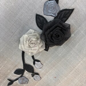 May include: A grey fabric background with a black and white floral applique. The applique features a large black rose, a smaller white rose, and three smaller white buds.