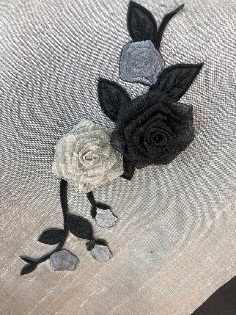 May include: A grey fabric background with a black and white floral applique. The applique features a large black rose, a smaller white rose, and three smaller white buds.