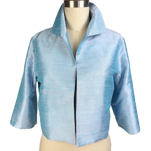 May include: A pale blue jacket with a wide collar and three-quarter length sleeves. The open-front design reveals the mannequin beneath. The fabric has a subtle sheen, suggesting silk or a similar material. The jacket is a stylish piece of outerwear.