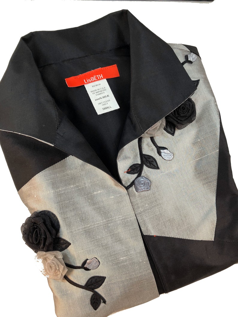 May include: A black and silver silk blouse with a black rose and leaf embroidery. The blouse has a collar and a button closure. The label reads "Lisbeth 100% Silk Dry Clean Only Small".