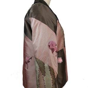K&ouml;nnte beinhalten: Eine braune, rosa und gr&uuml;ne Patchworkjacke mit Blumenschmuck. Die Jacke hat einen Kragen und lange &Auml;rmel.