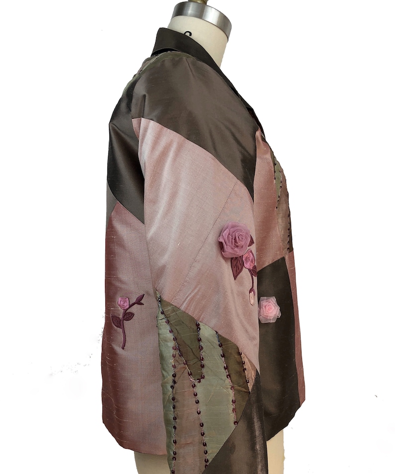 K&ouml;nnte beinhalten: Eine braune, rosa und gr&uuml;ne Patchworkjacke mit Blumenschmuck. Die Jacke hat einen Kragen und lange &Auml;rmel.