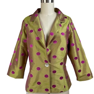 May include: A gold and fuchsia polka dot blazer with a single button fastening. The jacket features three-quarter length sleeves and a notched collar. The fabric has a subtle sheen, and the polka dots are evenly spaced.