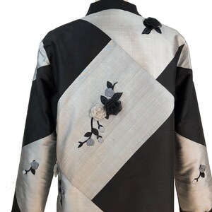 May include: A black and silver jacket with a diamond pattern and floral embroidery. The jacket has a mandarin collar and long sleeves.