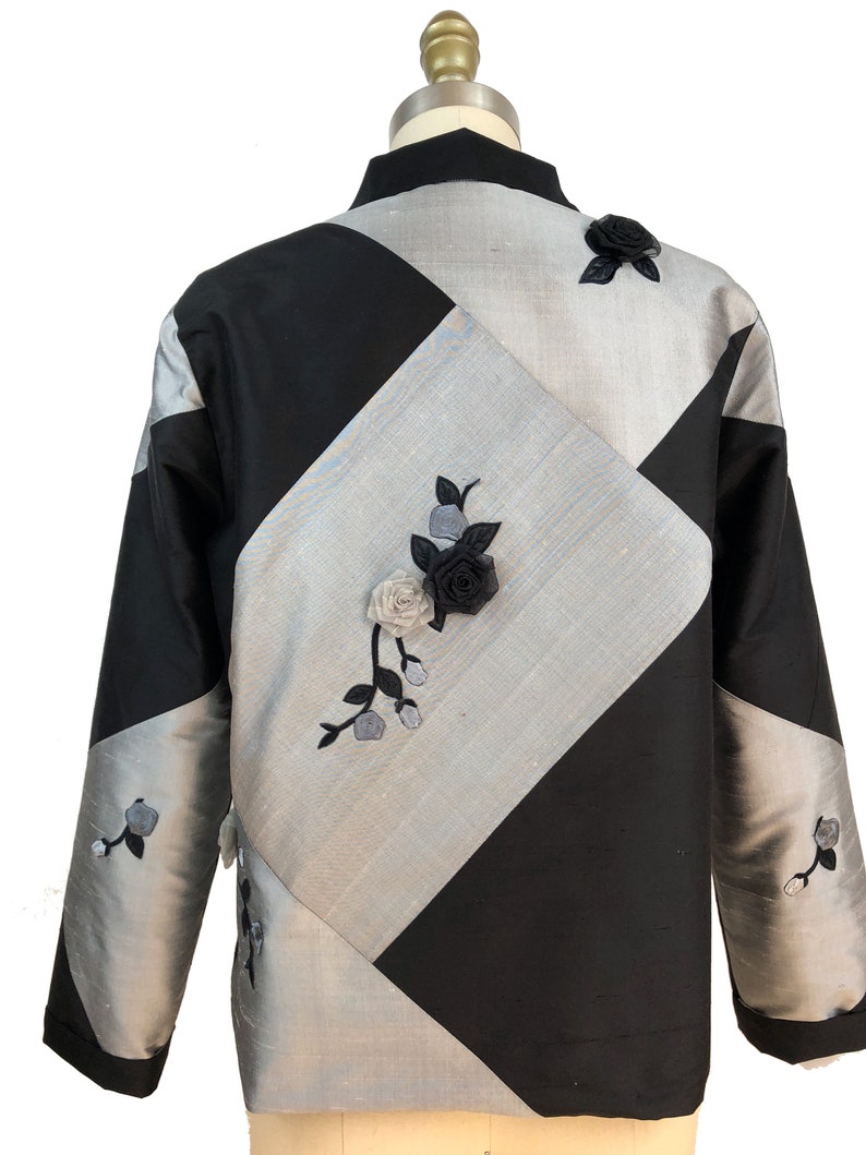 May include: A black and silver jacket with a diamond pattern and floral embroidery. The jacket has a mandarin collar and long sleeves.