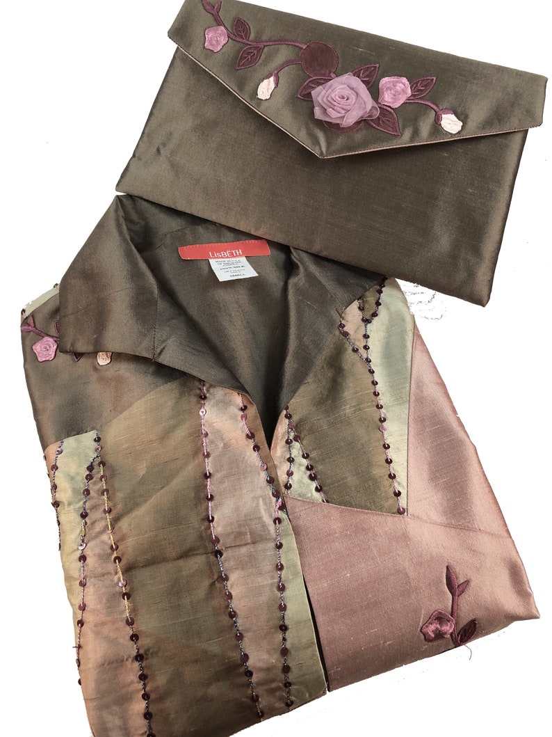 K&ouml;nnte beinhalten: Eine braune Seidenbluse mit einem rosa-gr&uuml;nen Blumendesign und eine passende braune Seidenclutch mit einem rosa Blumendesign. Die Bluse hat einen Kragen und einen Knopfverschluss. Die Clutch hat einen Klappenverschluss. Das Etikett "Lisbeth" ist auf der Bluse sichtbar.