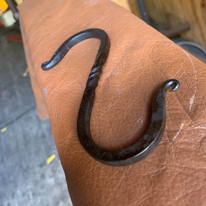 May include: A black metal hook with a twisted design. The hook is made of wrought iron and has a rustic finish.