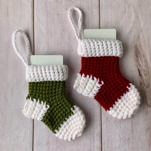 May include: Two small crocheted Christmas stockings with white trim and a white card inside each. One stocking is green and the other is red.