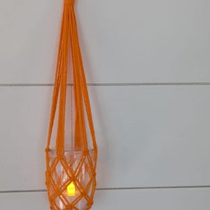 May include: Orange macrame hanging planter with a glass jar and a small light inside.