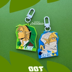 May include: Two 2.5 inch Ocarina of Time keychains. One features Link in his green tunic and the other features Sheik in their blue and white outfit. Both keychains have a silver metal ring.