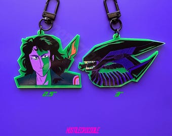 May include: Two fluorescent green acrylic keychains. One keychain features a green and purple anime character with the text "2.5" inches. The other keychain features a green and purple alien creature with the text "3" inches. The text "NOSTALGICROODLE" is printed in pink at the bottom of the image.