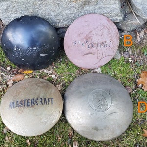 May include: Four vintage bowling balls rest on a bed of moss and fallen leaves. The balls are in various colors, including black, pink, and silver. Two balls have the text "Mastercraft" and one has the text "Ebonite" on them.