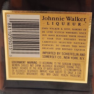 Pode incluir: Close-up de um r&oacute;tulo dourado em uma garrafa marrom de licor Johnnie Walker. O r&oacute;tulo apresenta texto preto detalhando o produto e um aviso governamental. A marca &eacute; proeminente.