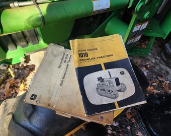 May include: Vintage John Deere 1010 Crawler Tractors service manuals. The manuals are yellowed with age and show signs of wear. The cover of one manual features a black and white illustration of a tractor. The manuals are resting on a green machine.