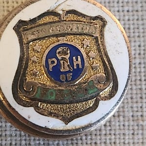 May include: A vintage gold-toned pin with a white border. The pin features a shield design with the text "PERPETUA" at the top, and "P&H OF CONCORD" at the bottom. The center has a blue circle with the letters "P&H".