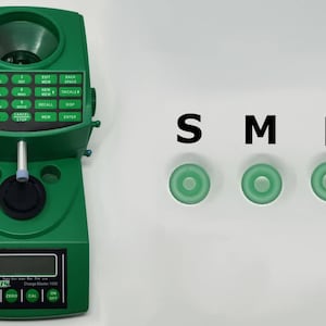 May include: A green reloading scale with a digital display and a keypad. The scale has a hopper on top and a powder measure on the side. The scale is labeled "RCBS Charge Master 1500". There are three green plastic rings labeled "S", "M", and "L".