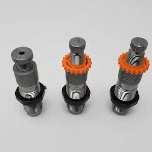 May include: Three silver reloading dies with orange rings. The die on the left has a black base. The die in the middle has the text "31L" on the top. The die on the right has a black base.