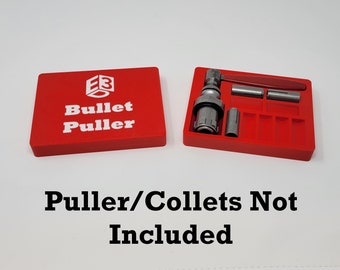 Può includere: Scatola di immagazzinaggio in plastica rossa con le parole "Bullet Puller" e un logo sul coperchio. La scatola è aperta per rivelare un estrattore di proiettili in metallo e diversi collettori in metallo.
