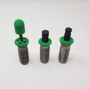 May include: Three reloading dies with green and black plastic tops. The dies are silver and have a threaded section. The top die has a green plastic knob.